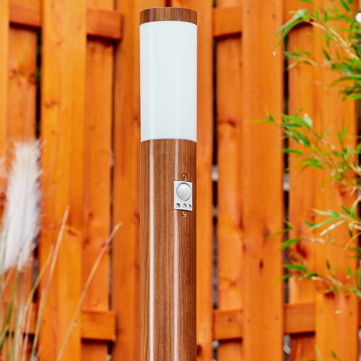 Eine hohe, zylindrische Außenlampe mit Holzmaserung und weißer Oberseite. In der Nähe eines Holzzauns platziert.