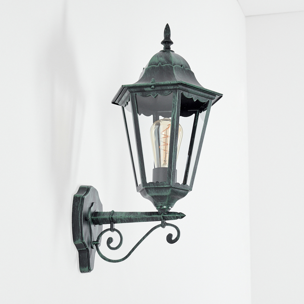 Wandlampe mit grünem Metallic-Finish und sichtbarer Glühbirne. Vor weißem Hintergrund.