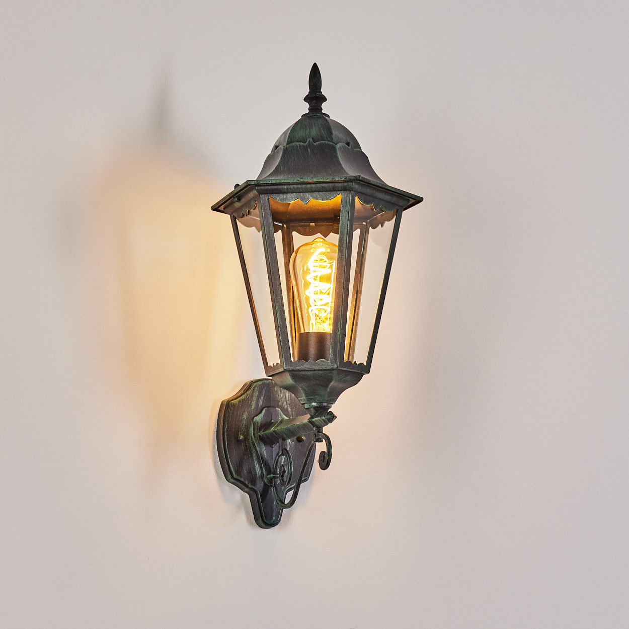 Wandlampe für den Außenbereich mit grünem Metallic-Finish und sichtbarer Glühbirne. Licht strahlt aus.