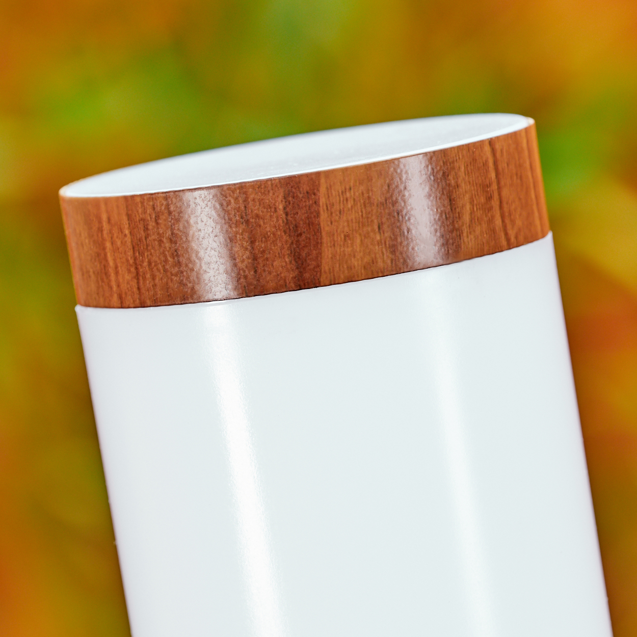 Nahaufnahme einer weißen und Holzlampe mit Holzoberteil. Verschwommener, farbenfroher Hintergrund.