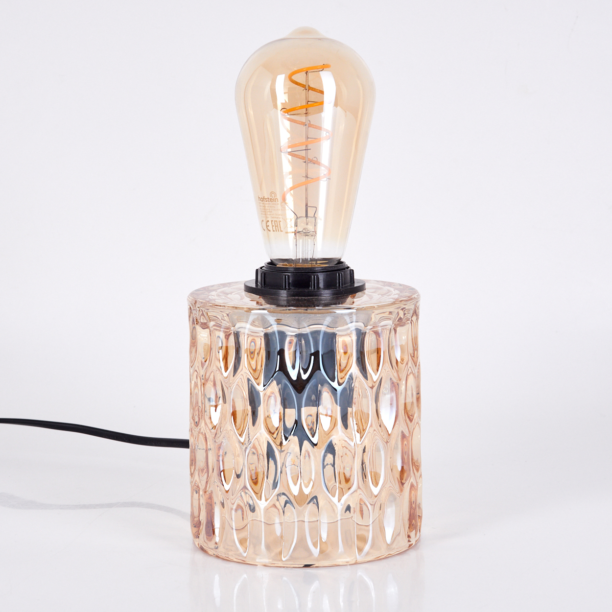 Eine Tischlampe mit strukturiertem bernsteinfarbenem Glasfuß und einer leuchtenden Glühbirne. Der Hintergrund ist weiß.