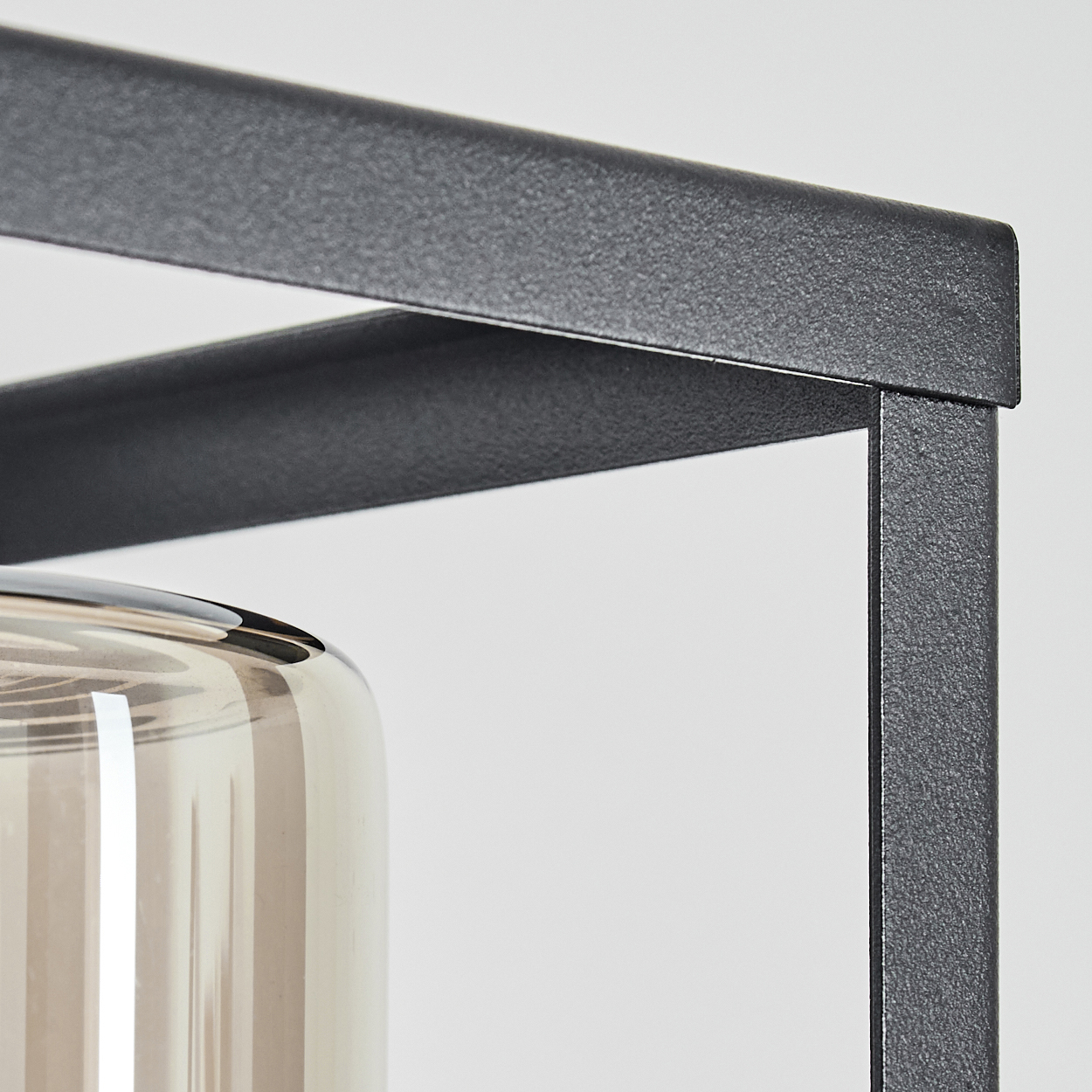 Nahaufnahme eines schwarzen Metallrahmens um eine Glasvase auf weißem Hintergrund.