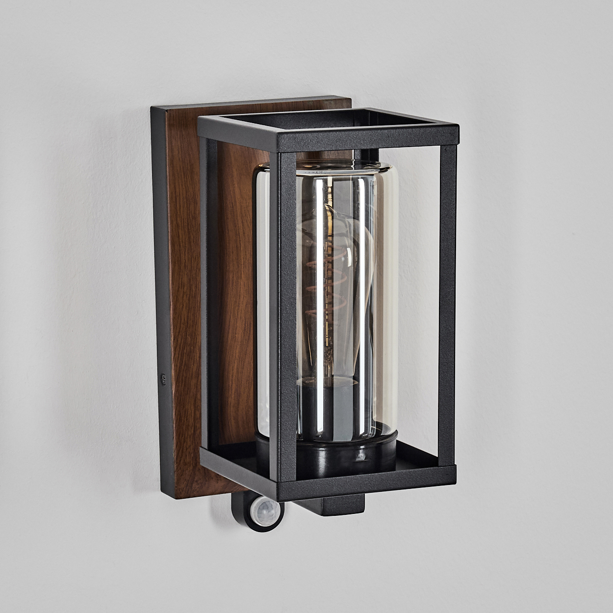 Wandleuchte mit schwarzem Metallrahmen, Holzrücken und Glaszylinder mit Glühbirne.