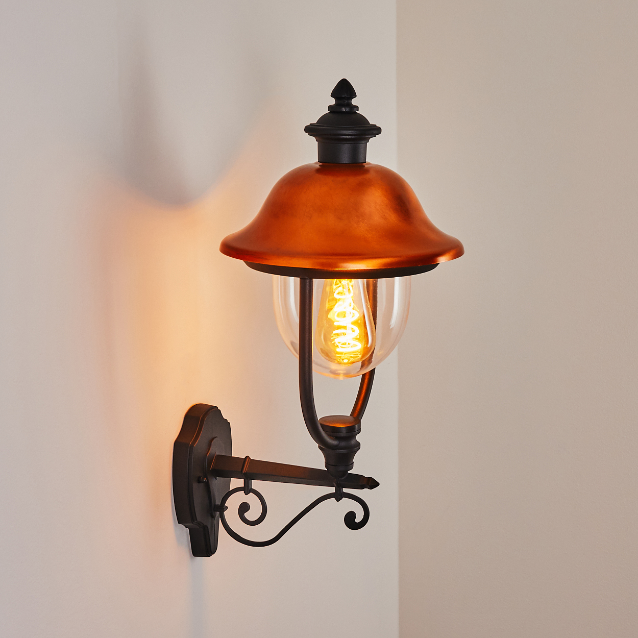 Außenlampe mit Kupferaufsatz und Glaskugel, am schwarzen Arm vor weißer Wand.