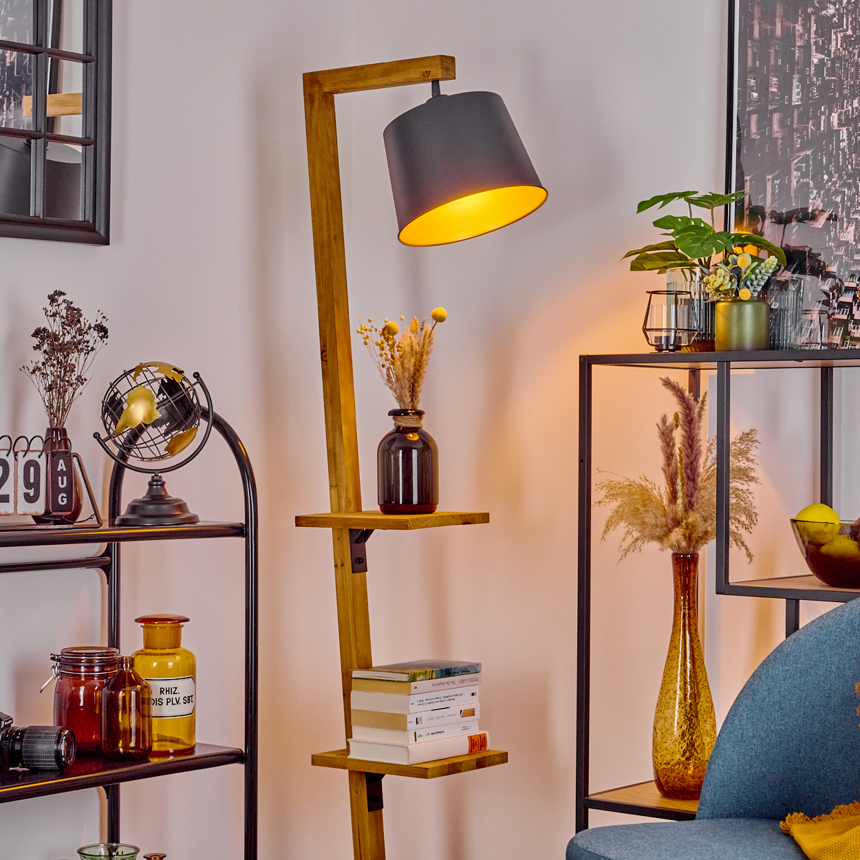 Eine Holz-Stehlampe mit schwarzem Lampenschirm und Regalen, platziert in einem Raum mit anderen Möbeln und Dekorationen.