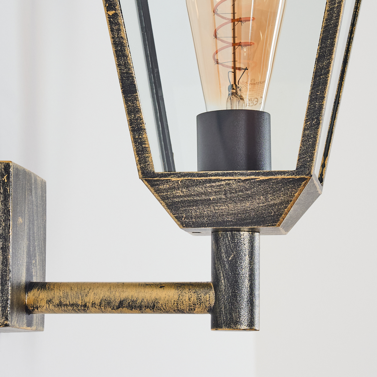 Nahaufnahme einer goldenen Wandlampe, die Details der Glühbirne und des Lampenrahmens zeigt.