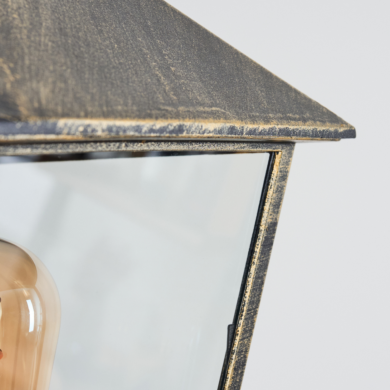 Nahaufnahme der Oberseite einer verzierten Außenlampe mit Glaspaneelen und Metallrahmen.