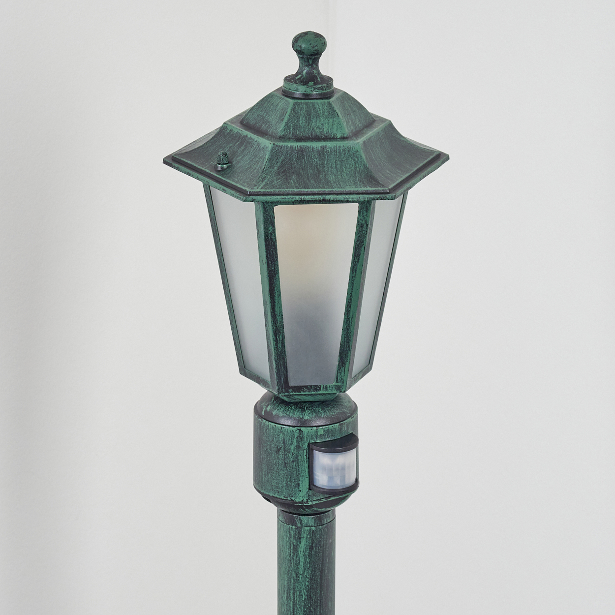 Grüne Außenlaterne mit Sensor. Die Lampe hat ein Milchglas und eine dekorative Spitze.