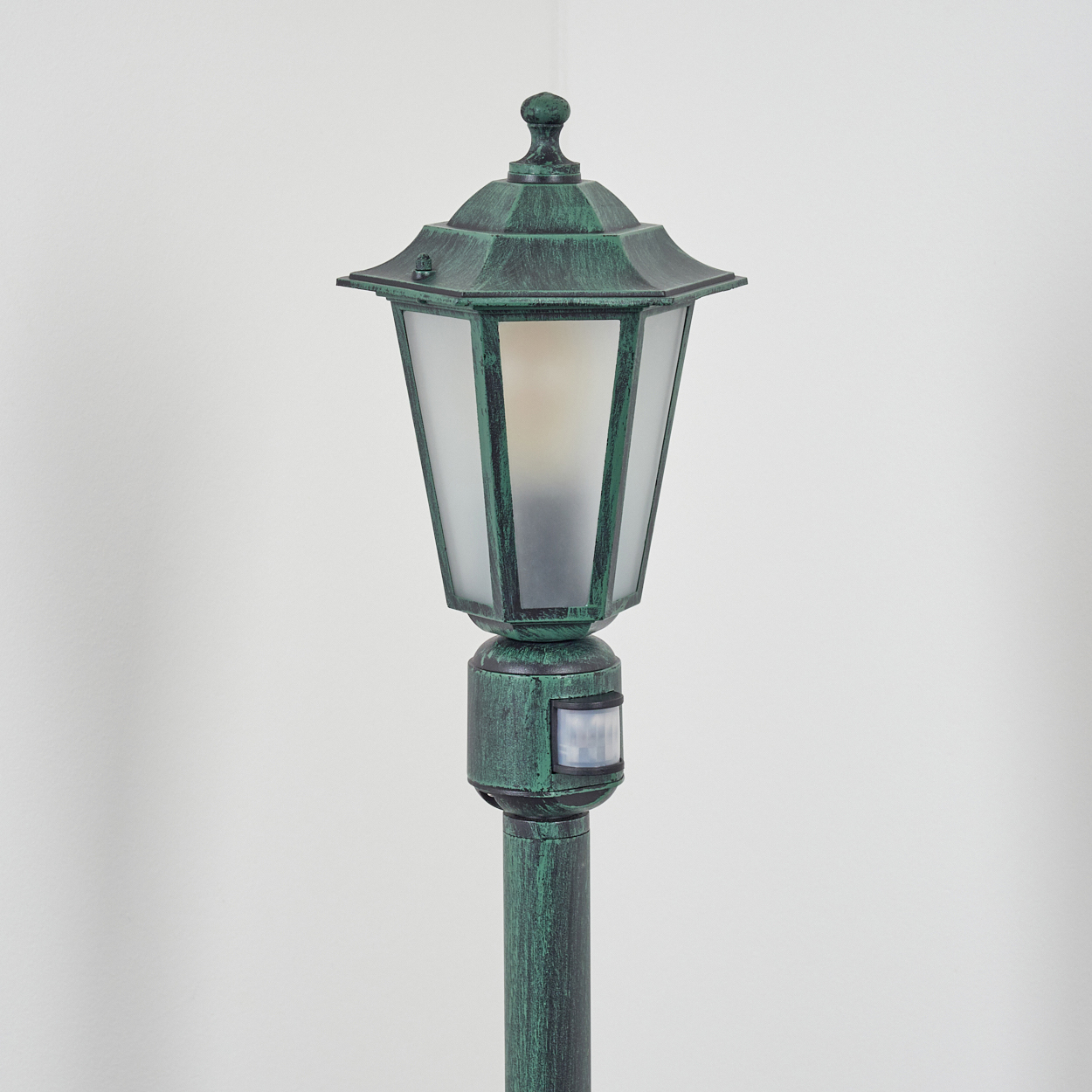 Grüne Außenlaterne mit Sensor. Die Lampe hat ein Milchglas und eine dekorative Spitze.