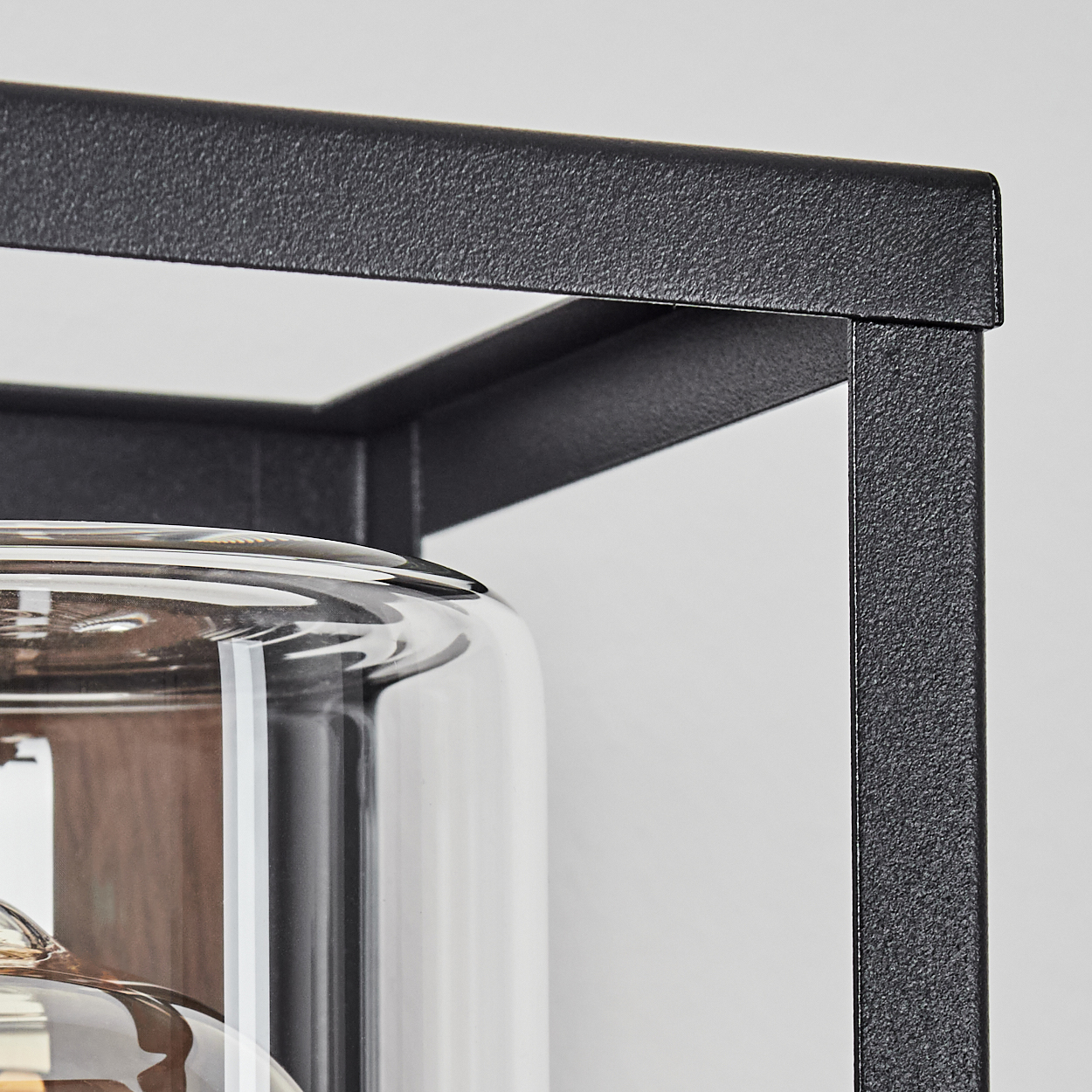 Nahaufnahme des schwarzen Rahmens einer Außenwandleuchte. Das Glas ist klar und der Rahmen hat eine strukturierte Oberfläche.