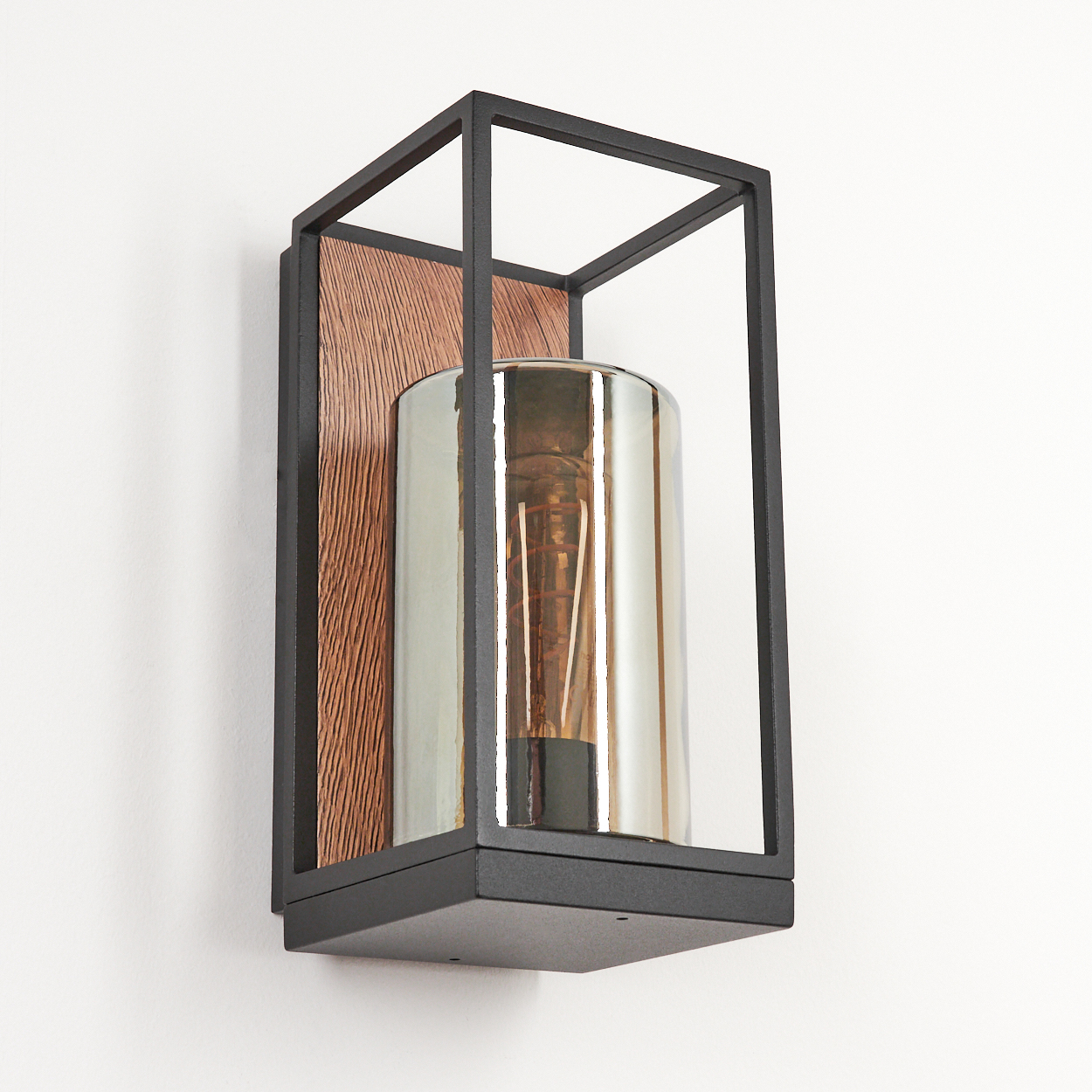 Wandlampe: schwarzer Rahmen, Holzrücken, Glaszylinder mit Glühbirne. Vor einer weißen Wand.