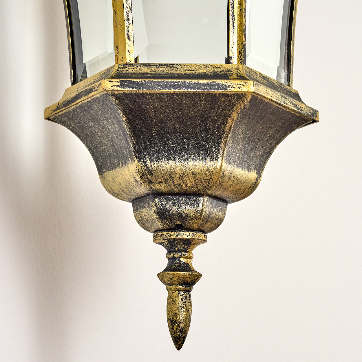Nahaufnahme des Bodens einer goldenen Wandleuchte mit dekorativem Sockel und klarem Glas.