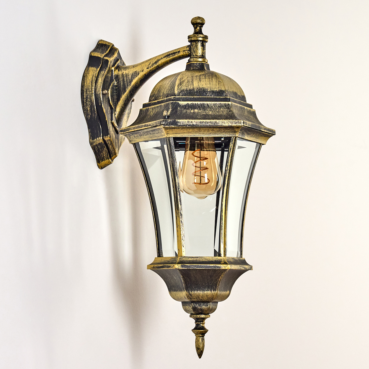 Goldene Wandlampe mit Klarglas. Sichtbare Glühbirne, an weißer Wand montiert.