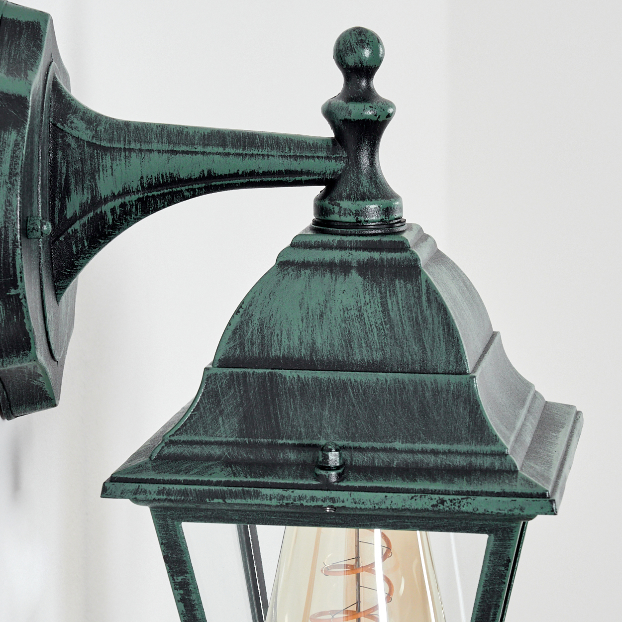 Nahaufnahme der grünen Wandlampe. Fokus auf der dekorativen Oberseite und dem Glas der Lampe.