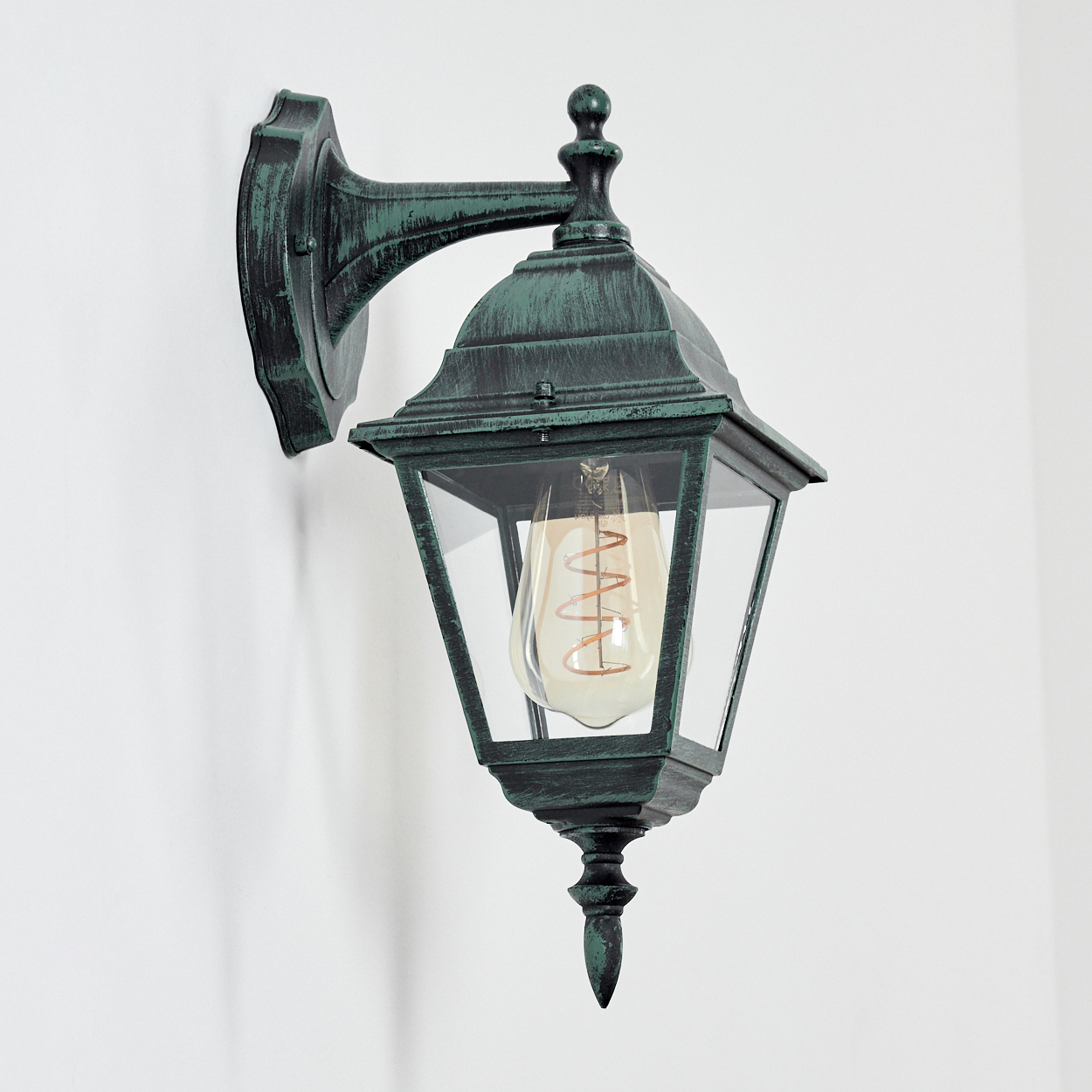 Grüne Wandlampe mit Klarglas und Glühbirne. An einer weißen Wand montiert.