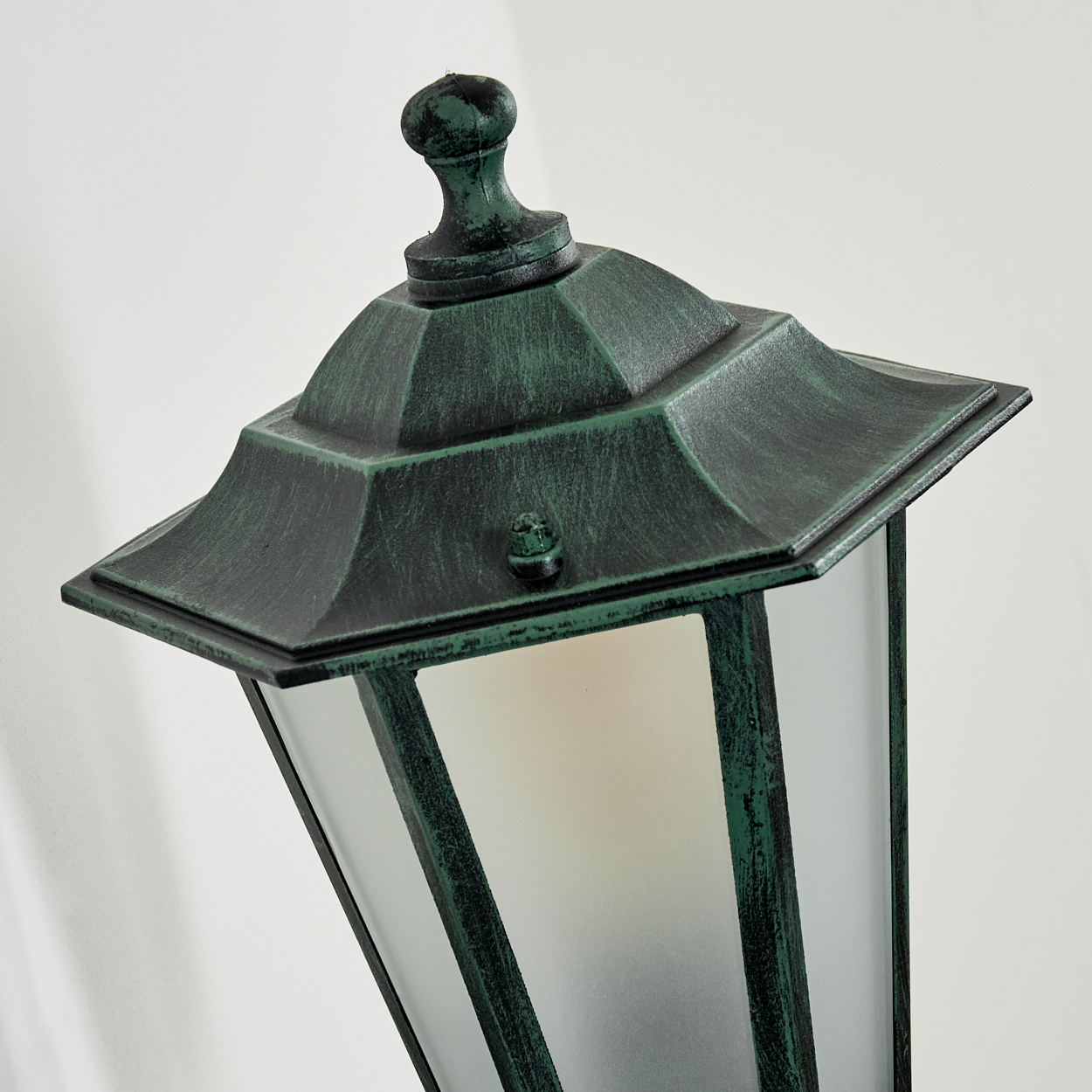 Nahaufnahme einer grünen Außenlampe. Die Lampe hat ein Milchglas und eine dekorative Oberseite.