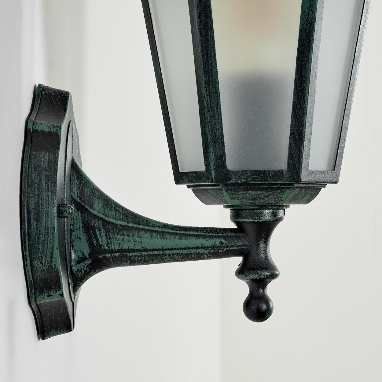 Eine grüne Außenlampe, die an einer Wand montiert ist. Die Lampe hat einen dekorativen Arm und Milchglas.