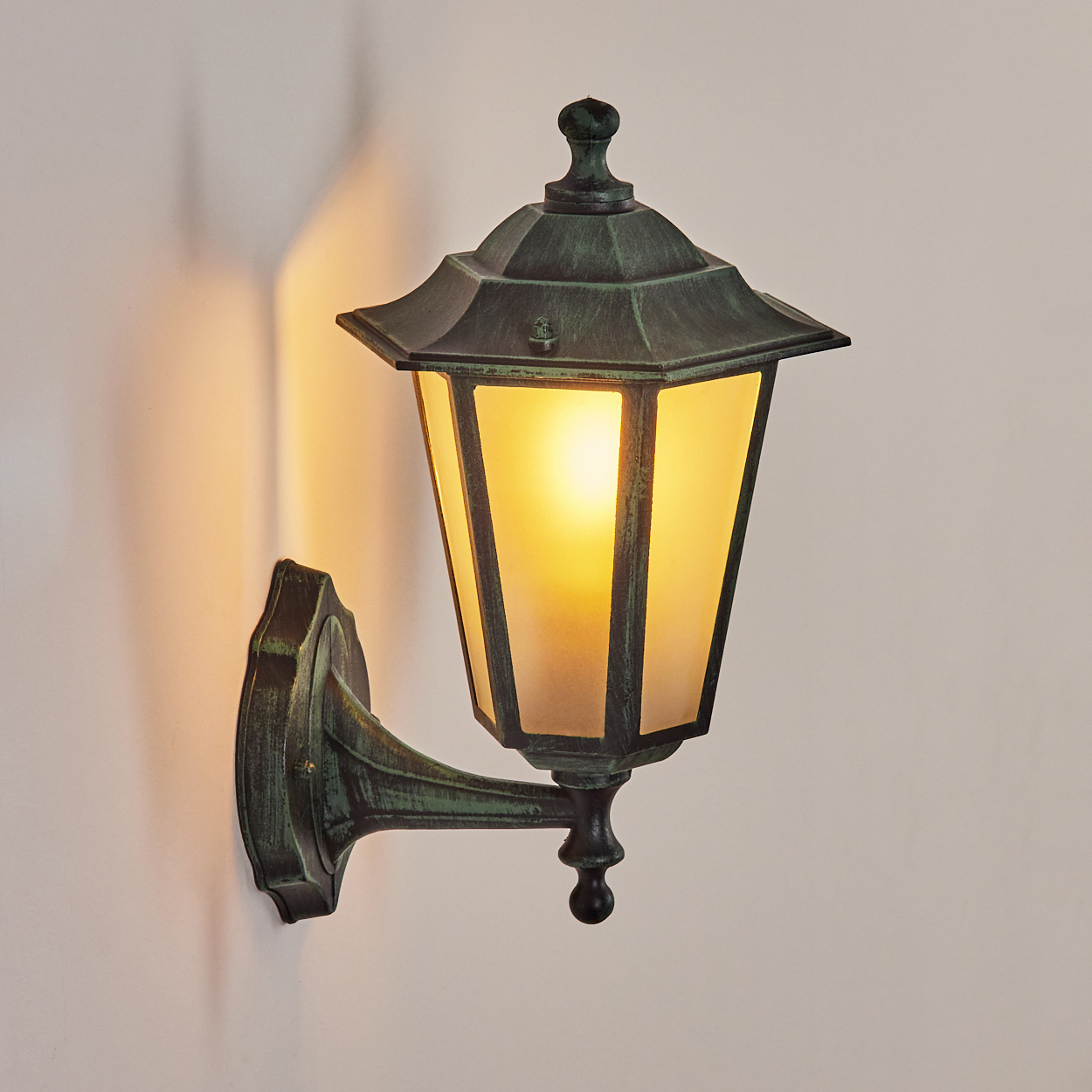 Eine grüne Wandleuchte mit beleuchtetem, mattiertem Glas. Die Lampe ist an einer hellen Wand befestigt.