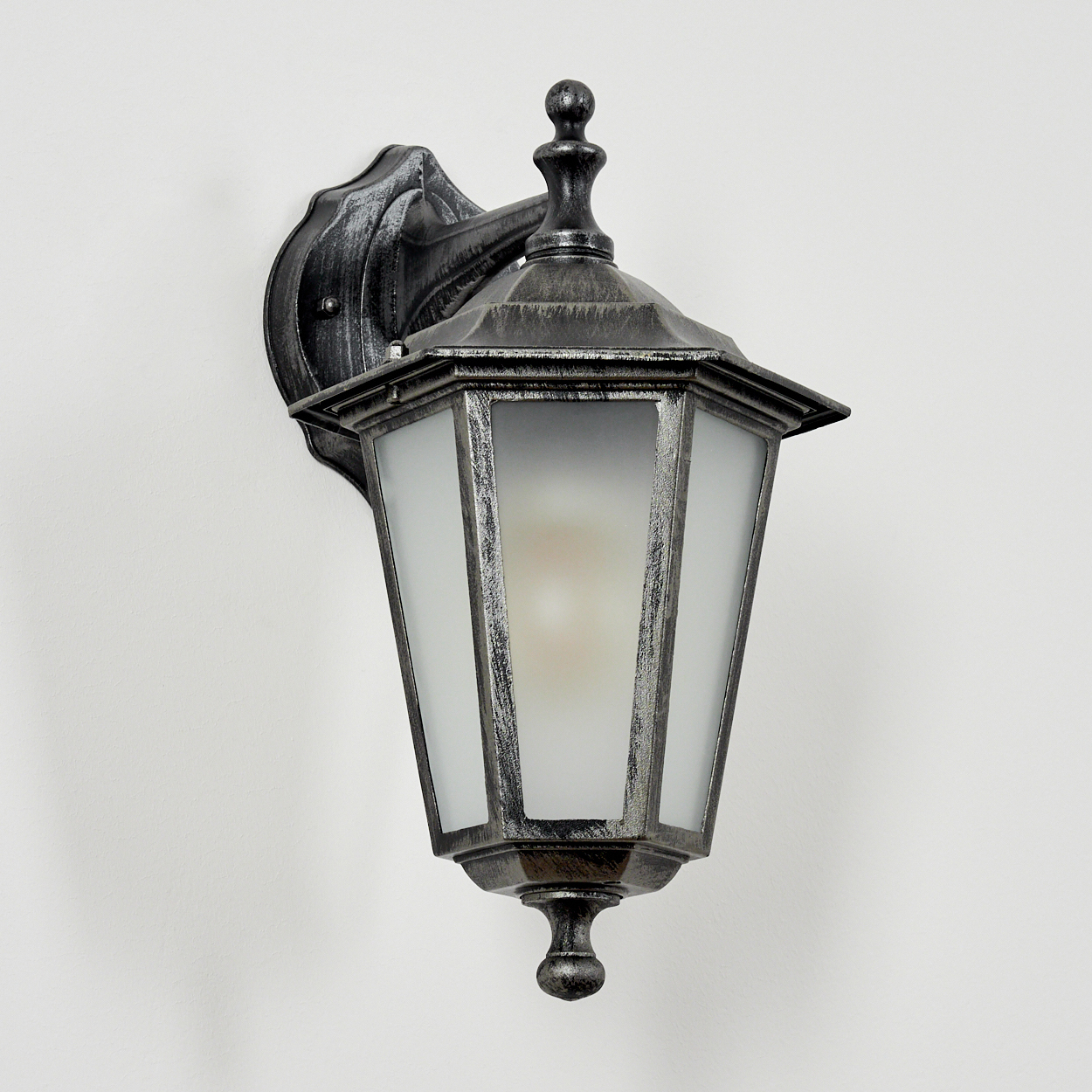 Eine Außenwandleuchte mit Metallic-Finish und Milchglas, an einer weißen Wand montiert. Seitenansicht.
