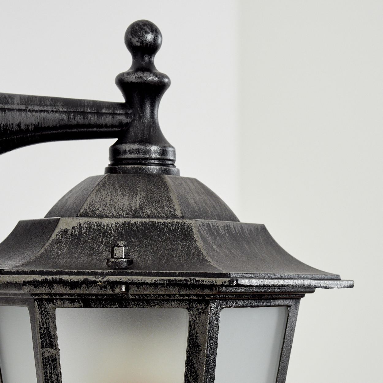 Nahaufnahme einer schwarzen Außenlampe mit Milchglas und gealterter Oberfläche vor weißer Wand.