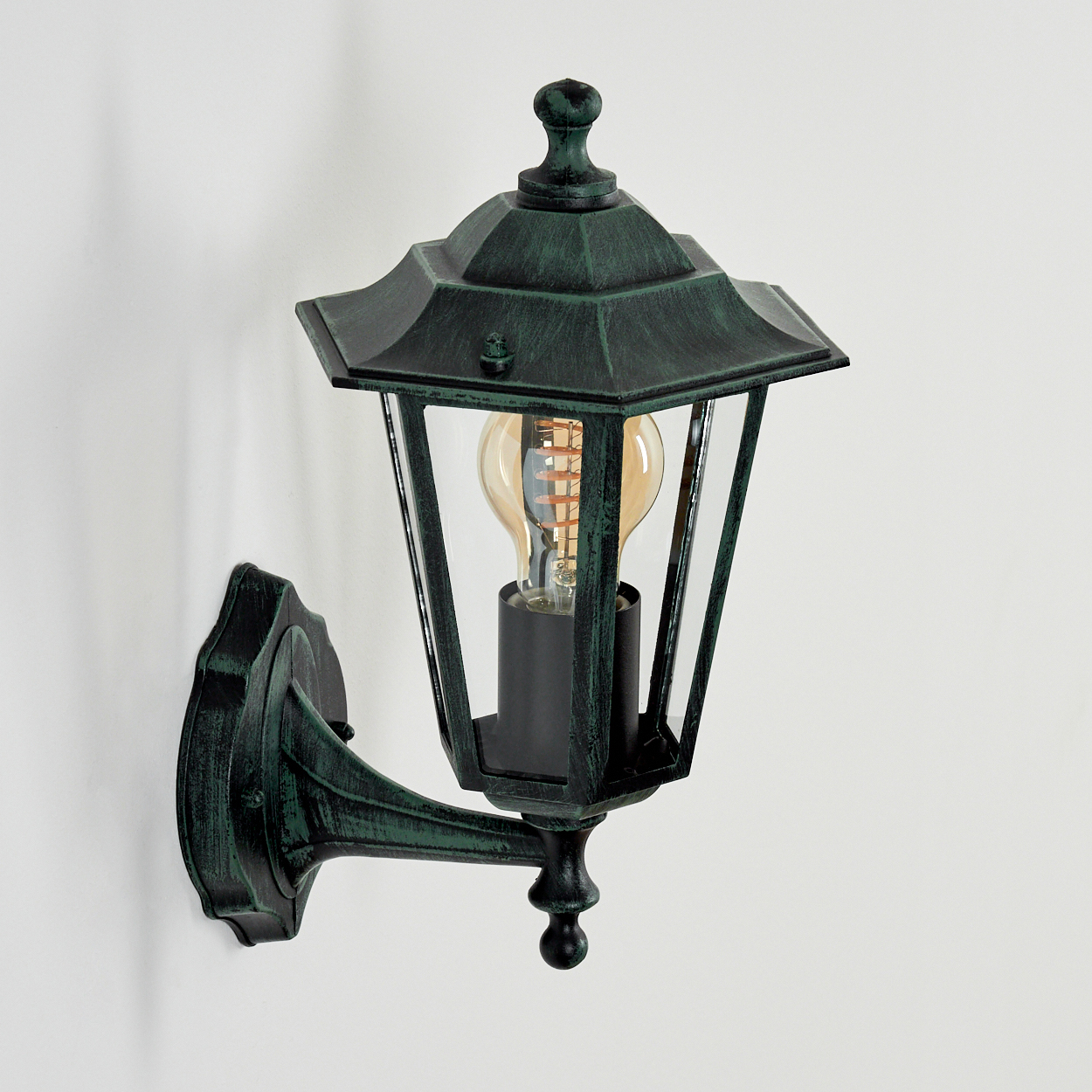 Eine grüne Wandlampe mit freiliegender Glühbirne. Sie ist an einer weißen Wand befestigt.