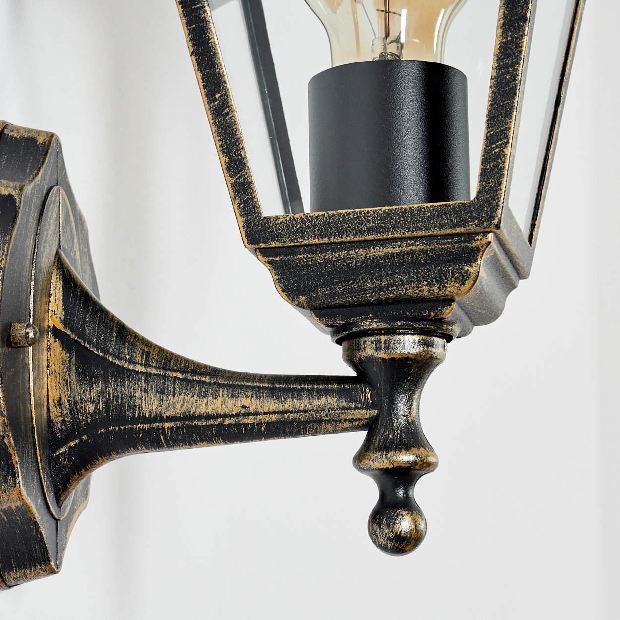 Nahaufnahme der Basis einer Außenlampe, mit sichtbarer Glühbirne, schwarz-goldener Oberfläche.