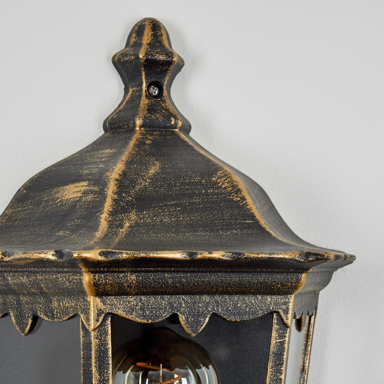 Nahaufnahme einer goldenen und schwarzen Lampenspitze mit leuchtender Glühbirne. An weißer Wand.