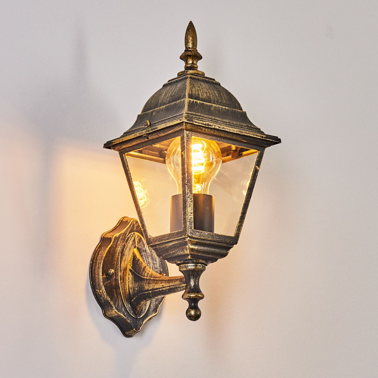 Wandlampe, schwarz-gold, mit leuchtender Glühbirne, auf weißem Hintergrund.
