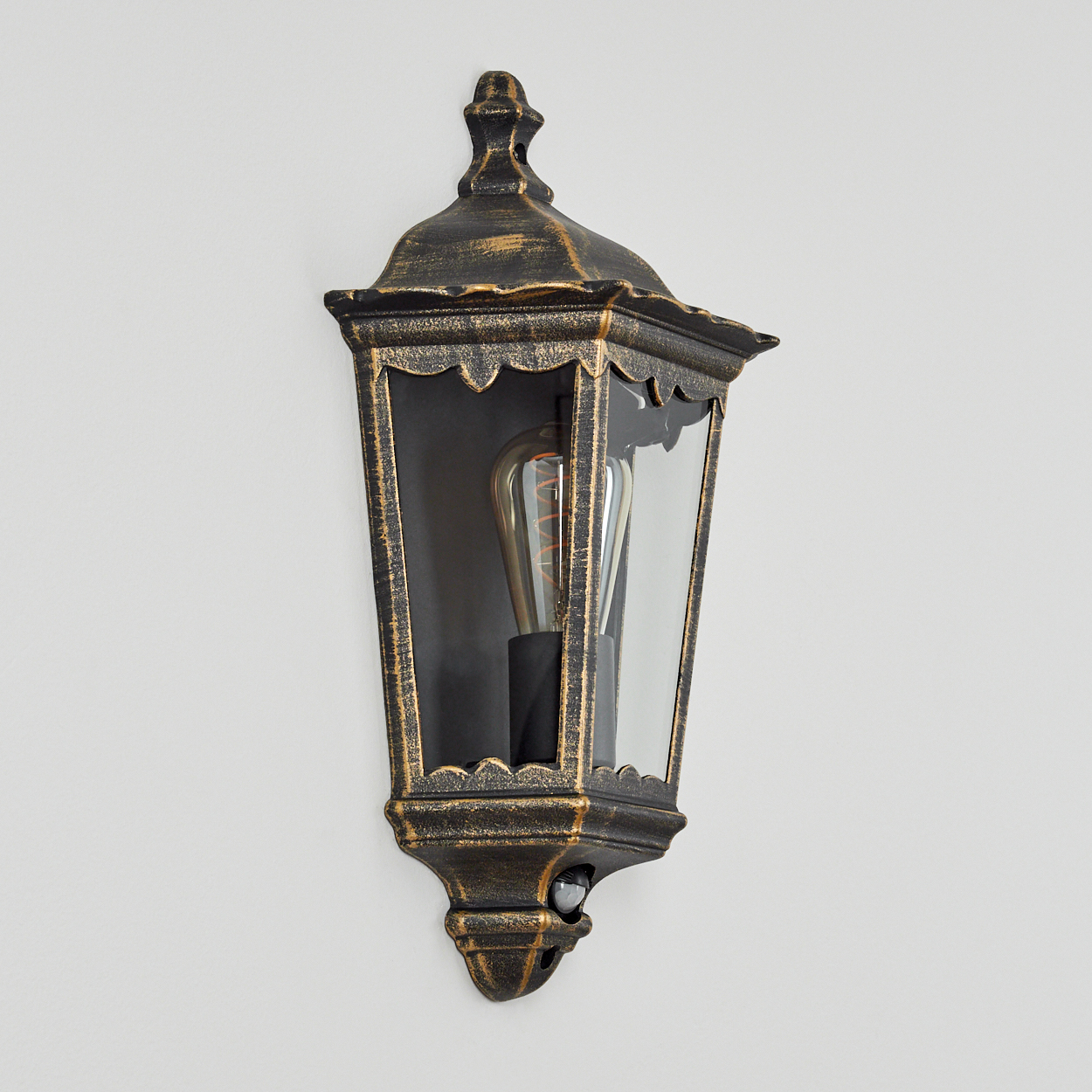 Goldene und schwarze Wandlampe mit leuchtender Glühbirne. An weißer Wand montiert. Mit Sensor.