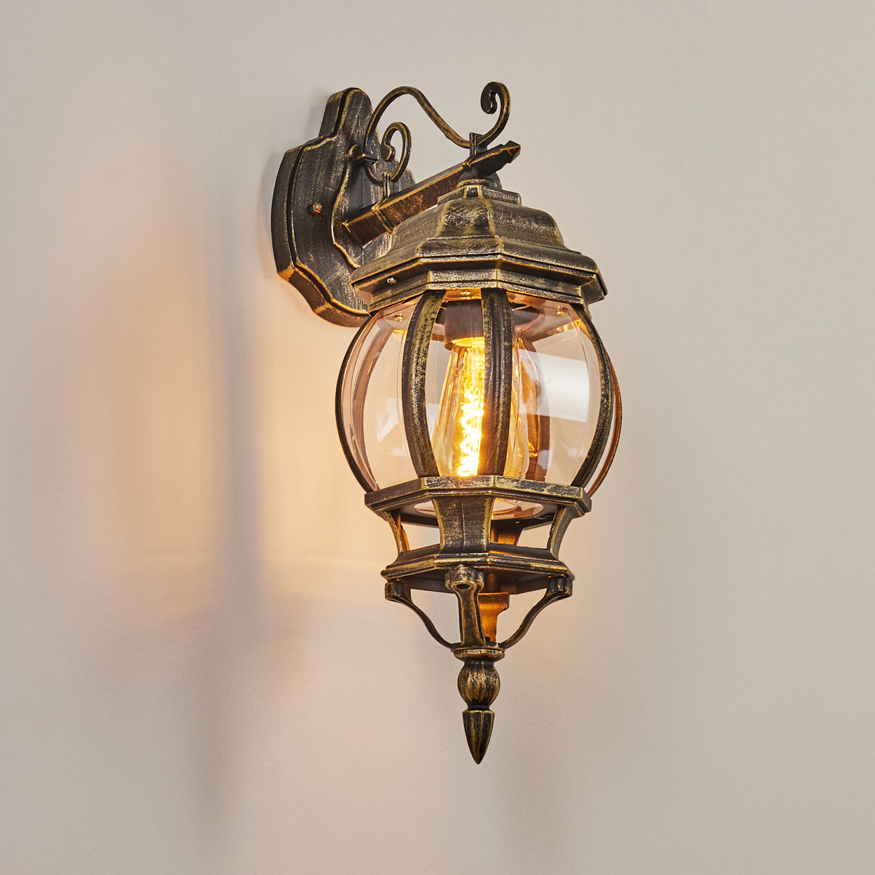 Goldene Metall-Wandleuchte mit Glühbirne an einer weißen Wand.
