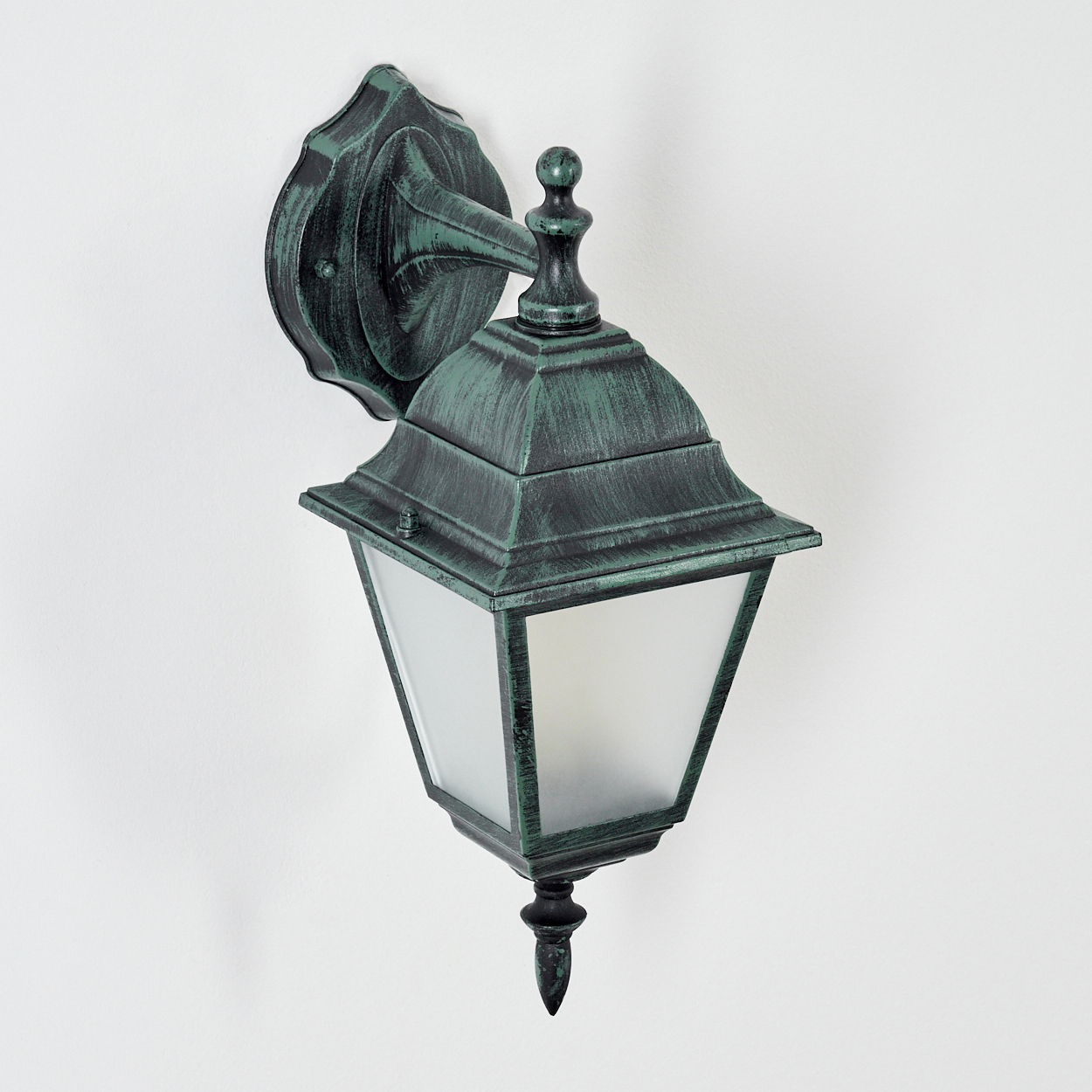 Eine grüne Außenlampe an einer weißen Wand montiert. Die Lampe hat eine dekorative Spitze und klare Glasscheiben.