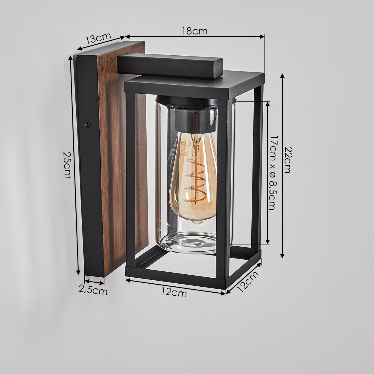 Eine Wandlampe mit Maßen. Sie hat eine Holzrückseite, einen schwarzen Rahmen, einen Glaszylinder und eine warme Glühbirne.