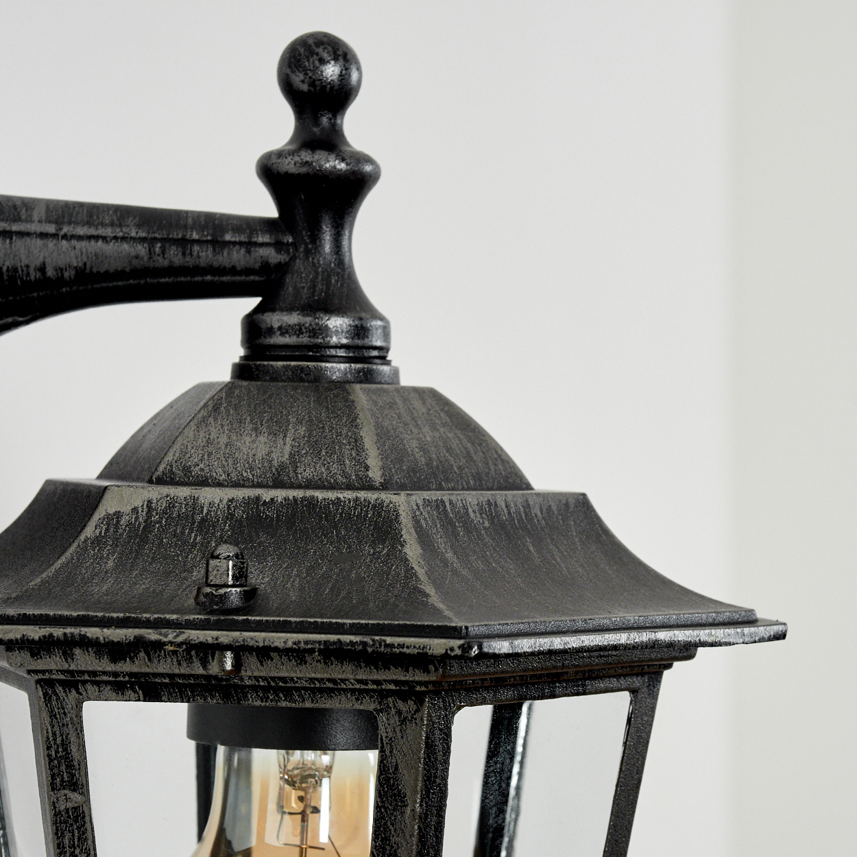 Nahaufnahme einer Außenlampe mit dekorativer Spitze und klaren Glasscheiben. Eine Glühbirne ist sichtbar.