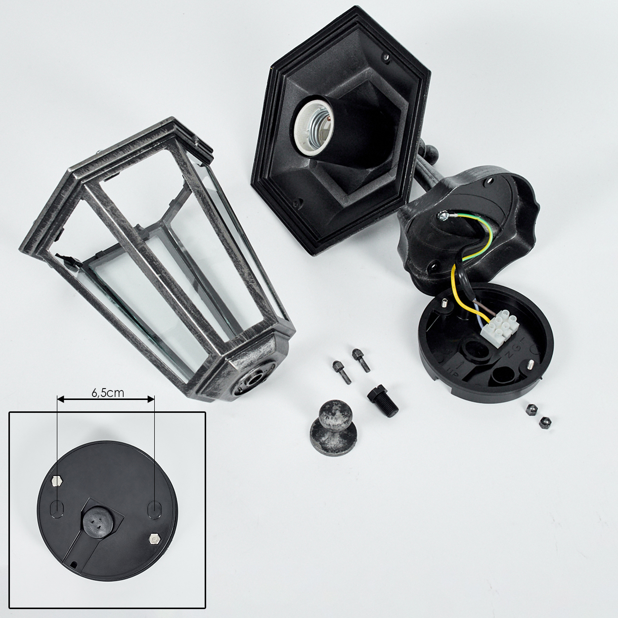 Zerlegte schwarz-silberne Wandlampe mit einem Glaskasten und verschiedenen Komponenten auf Weiß.