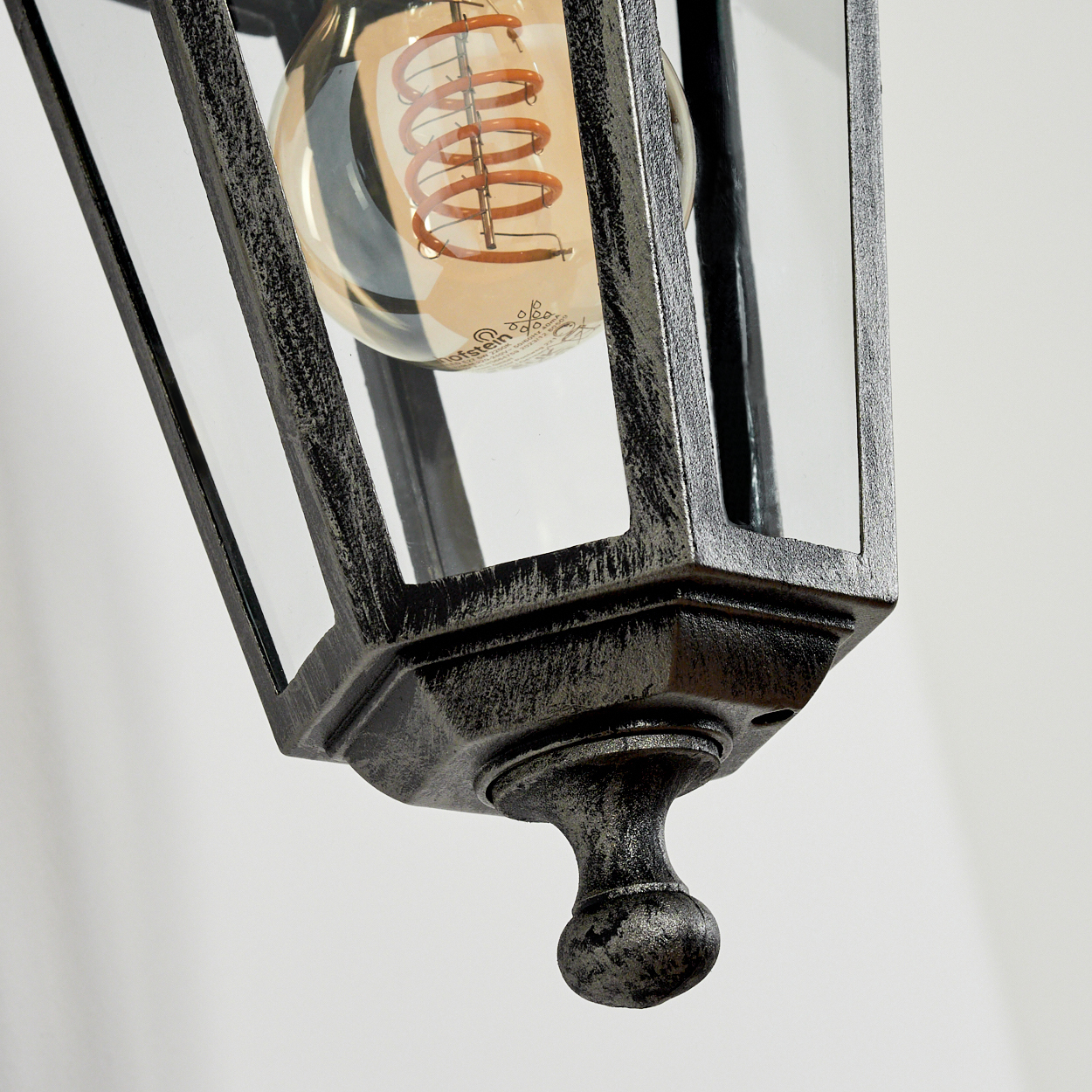Nahaufnahme einer leuchtenden Glühbirne in einer Außenleuchte, wobei die Metalldetails sichtbar sind.