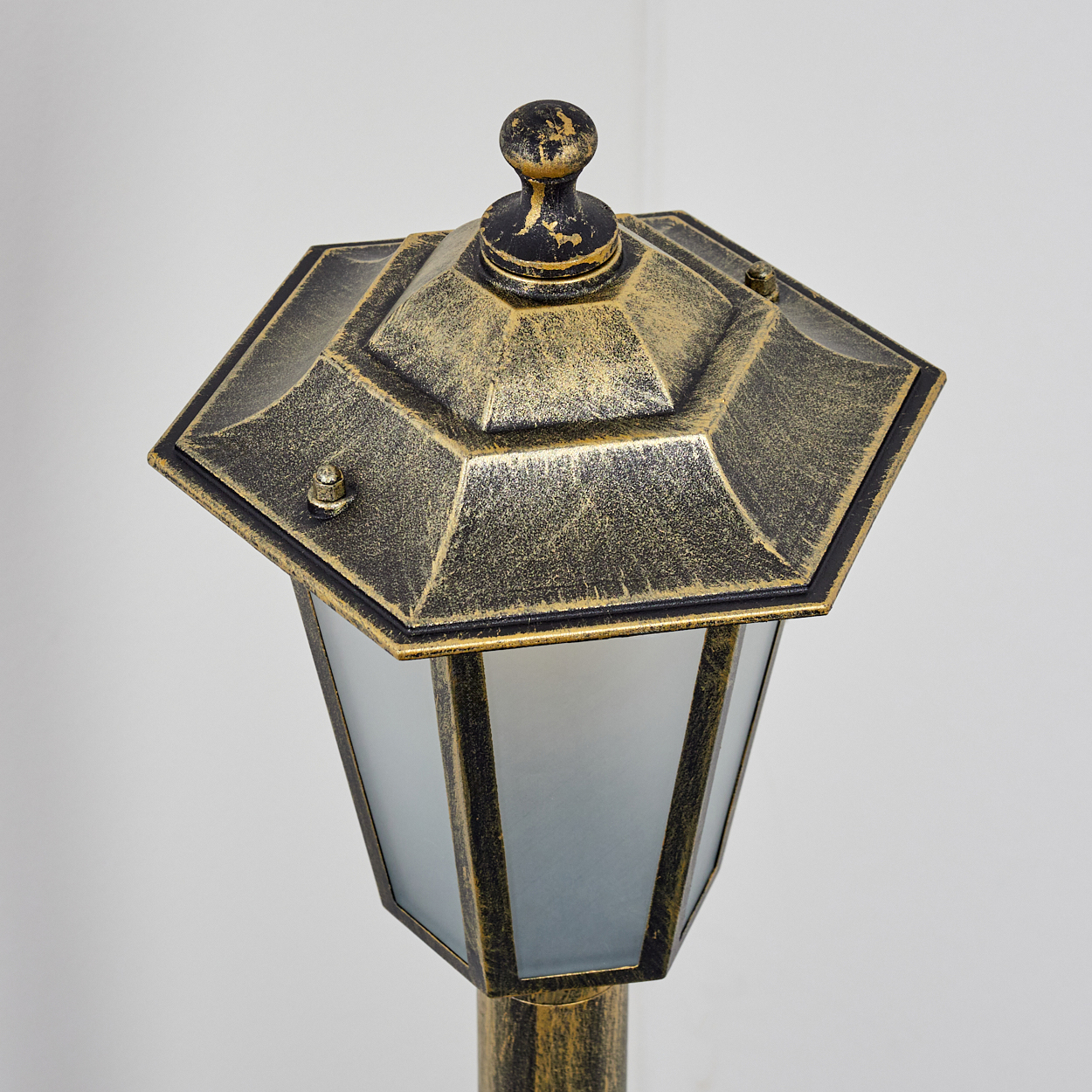 Eine gold-schwarze sechseckige Außenlampe mit Milchglasscheiben, Draufsicht.