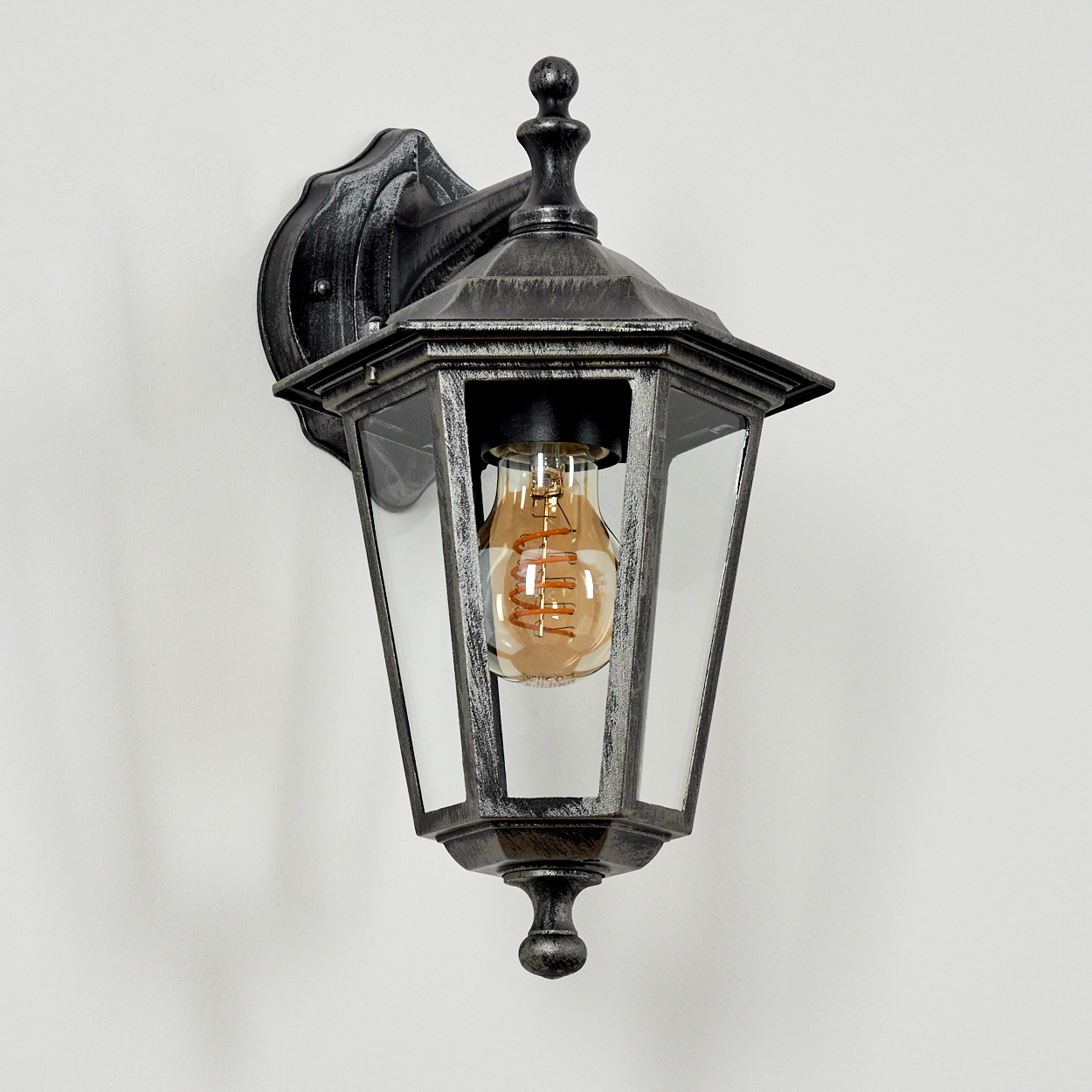 Außenlampe an einer weißen Wand montiert. Die Lampe hat eine dekorative Spitze und klare Glasscheiben.