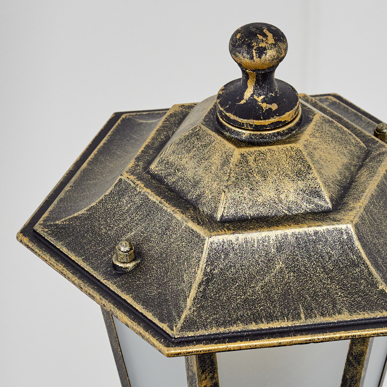 Nahaufnahme der Oberseite einer gold-schwarzen Außenlampe mit dekorativem Zierknauf.