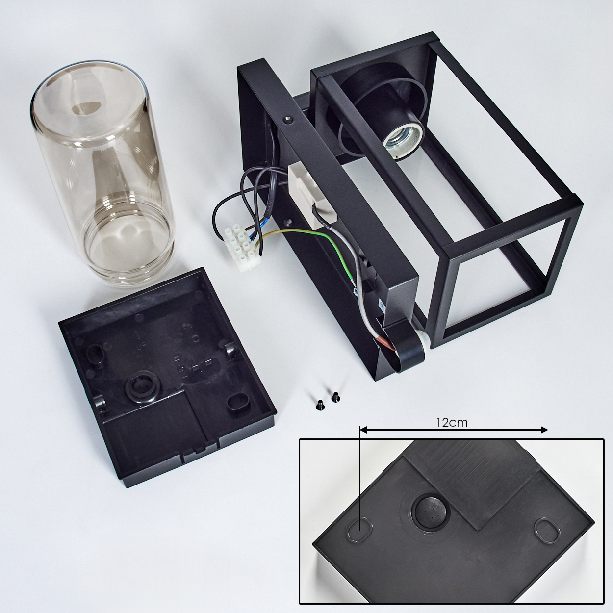 Zerlegte Lampe mit schwarzen Teilen, Drähten und Glaszylinder auf weißer Oberfläche.