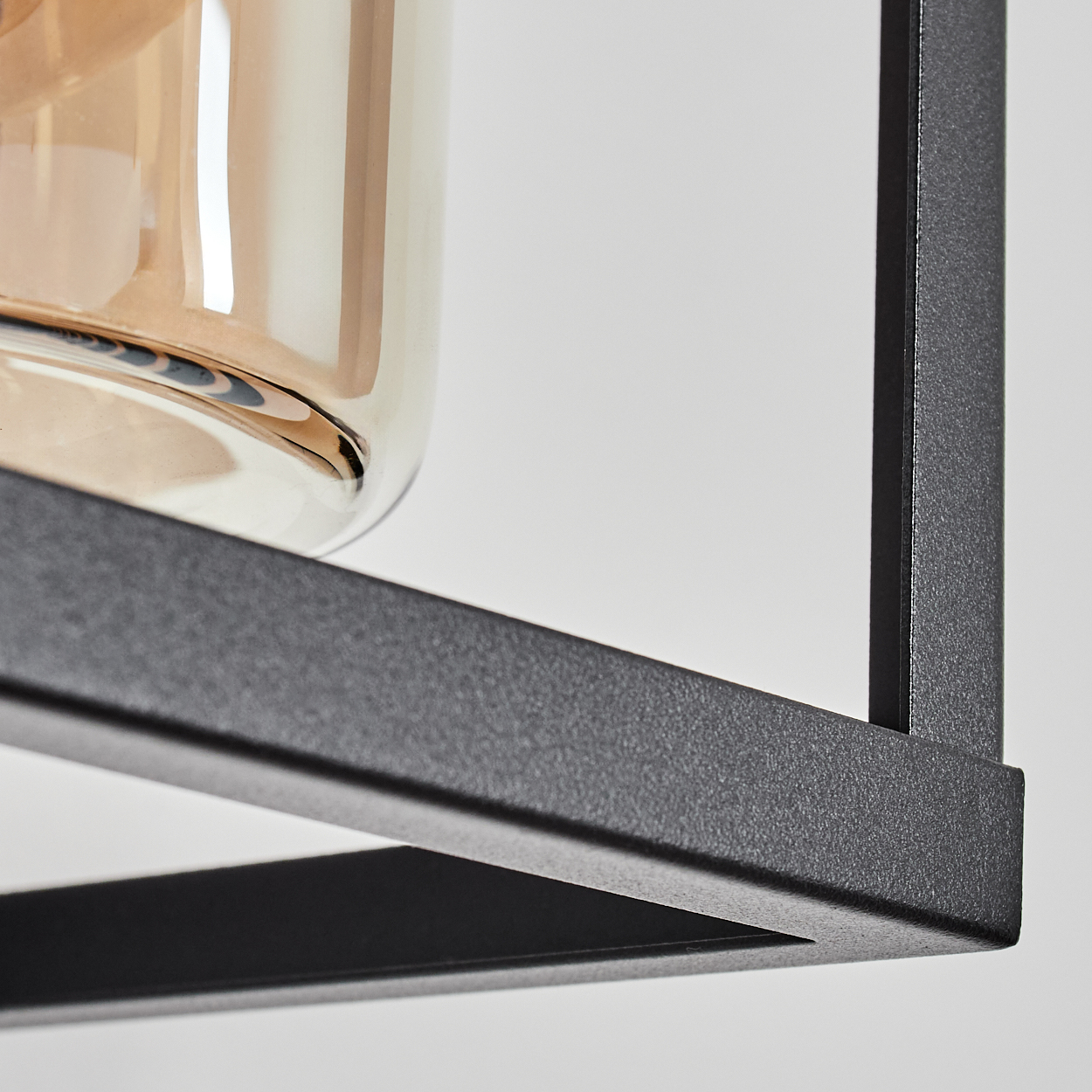 Nahaufnahme des schwarzen Rahmens einer Wandlampe mit einem Glaszylinder und einer Glühbirne.