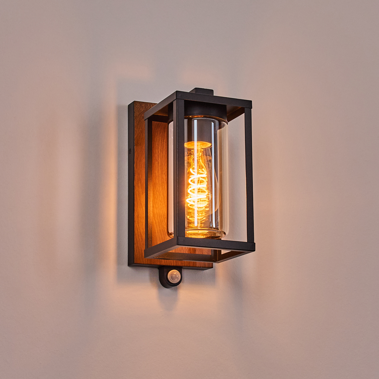 Eine beleuchtete Wandlampe mit einer Glühbirne in einem Glaszylinder, an einem Holzbrett befestigt.