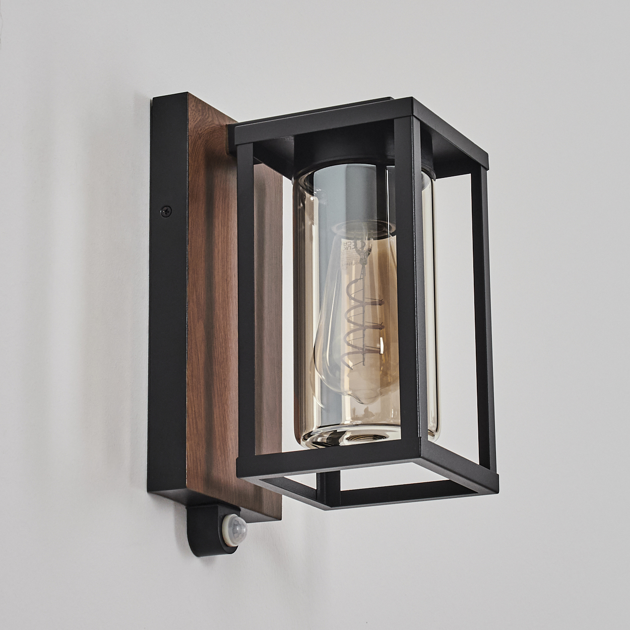 Wandlampe mit Holzsockel, schwarzem Rahmen, Glaszylinder und Glühbirne.