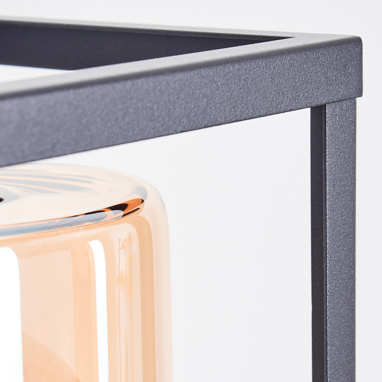 Nahaufnahme des schwarzen Rahmens einer Wandlampe und eines Glaszylinders mit einer orangefarbenen Glühbirne.