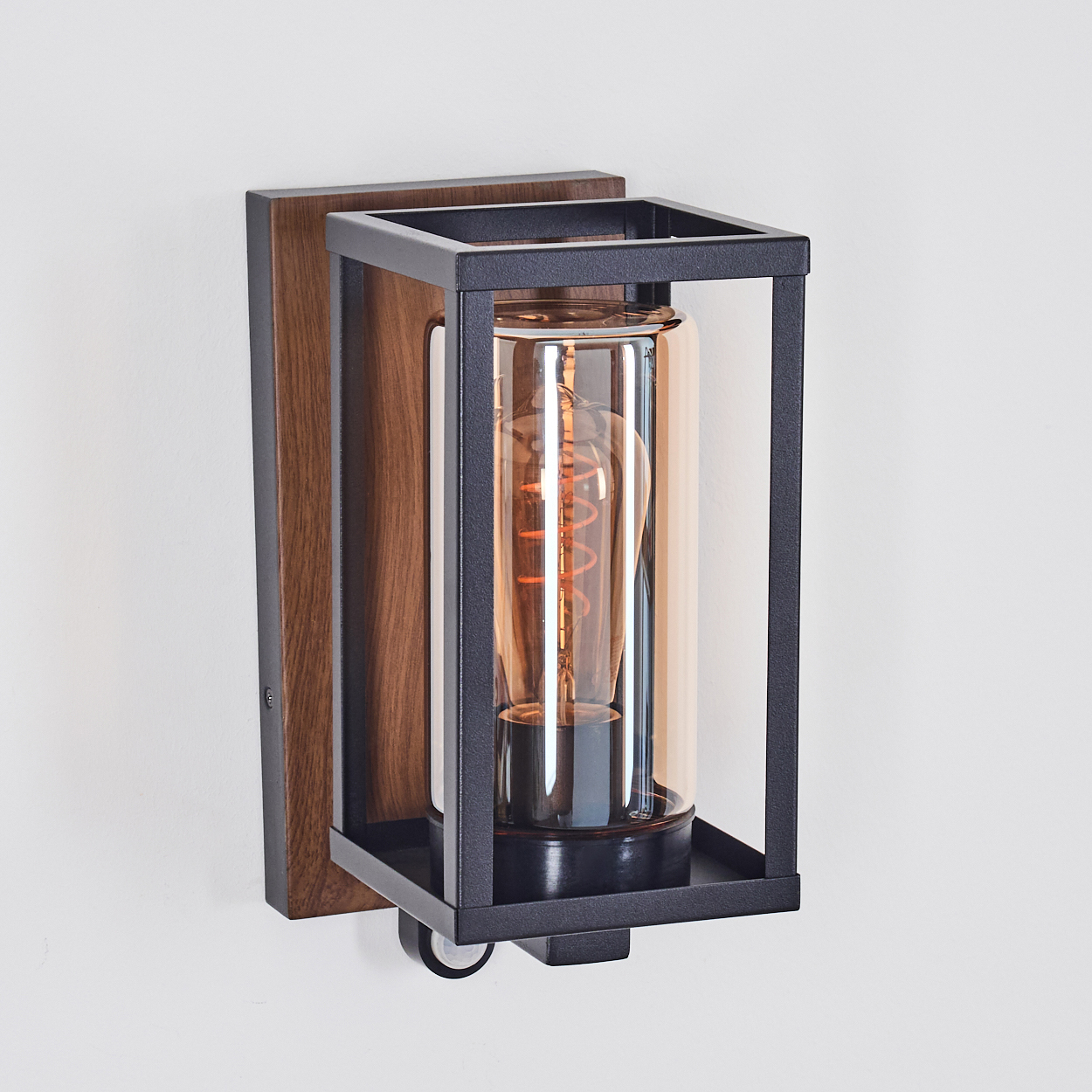 Schwarze Außenlampe mit Holzrückwand und klarem Glaszylinder. Glühbirne innen sichtbar.
