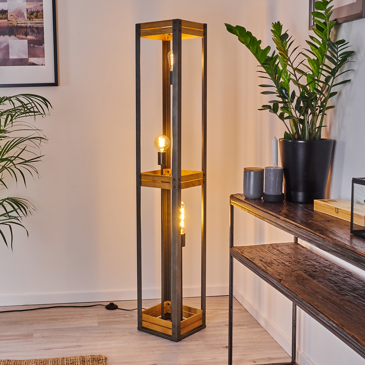 Hohe Holzlampen mit drei freiliegenden Glühbirnen. Sie steht in einem Raum mit Pflanzen und einem Tisch.
