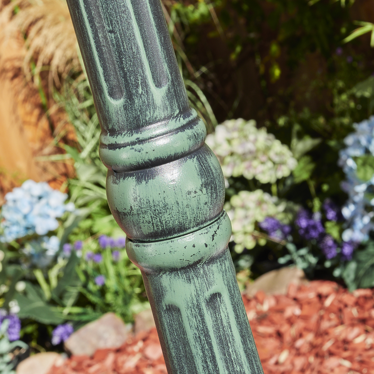 Nahaufnahme eines Abschnitts einer grünen Laterne, zeigt strukturiertes Design und verschwommenen Gartenhintergrund.