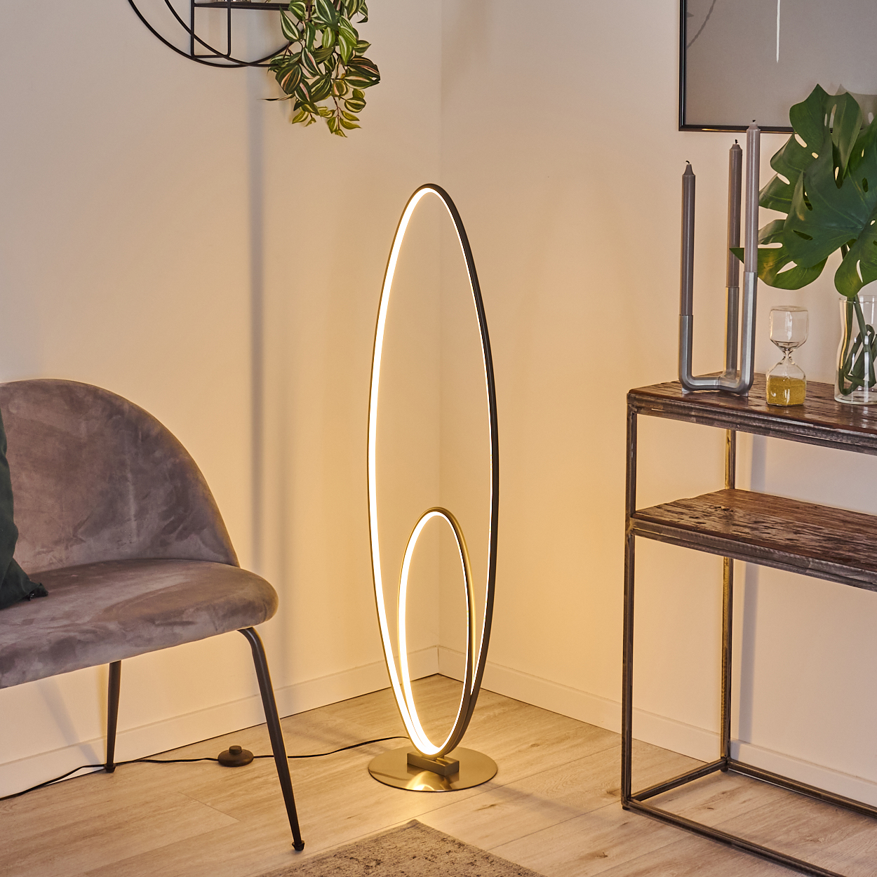 Eine hohe, ovale Stehleuchte in einem Raum mit Stuhl, Tisch und Pflanzen. Die Lampe ist an.