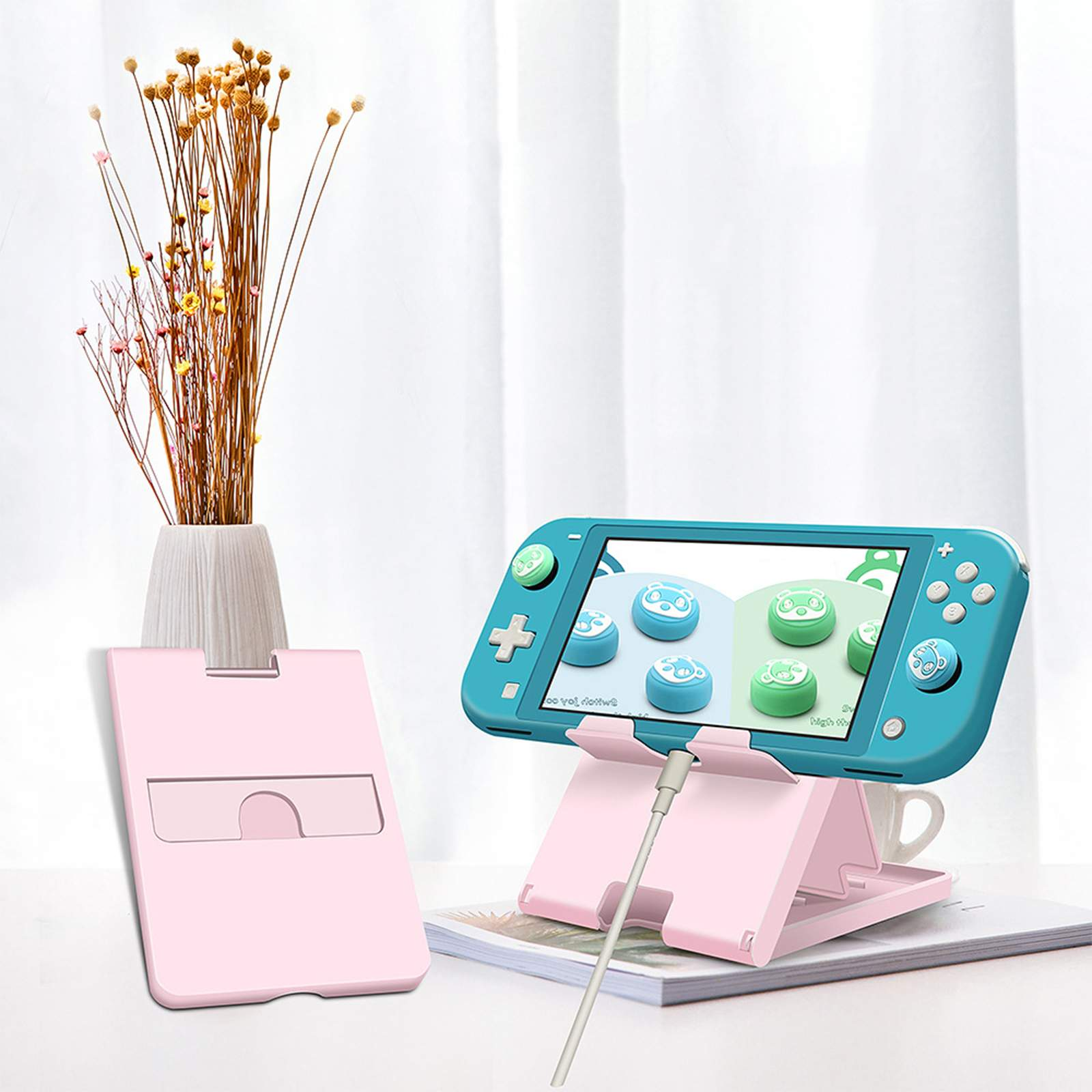 Eine türkisfarbene Handheld-Konsole auf einem Ständer, mit einem rosa Kartenhalter und einer Blumenvase.