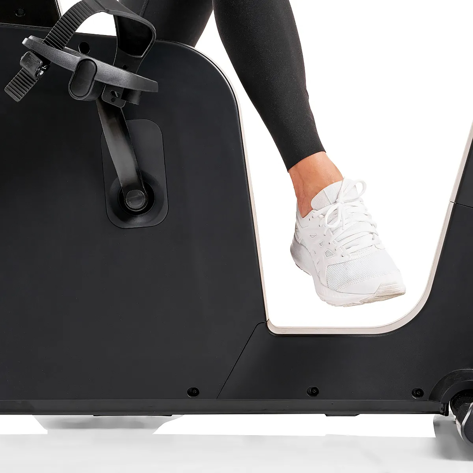 Bein und Fuß einer Person in einem weißen Sneaker auf einem schwarzen Heimtrainer.
