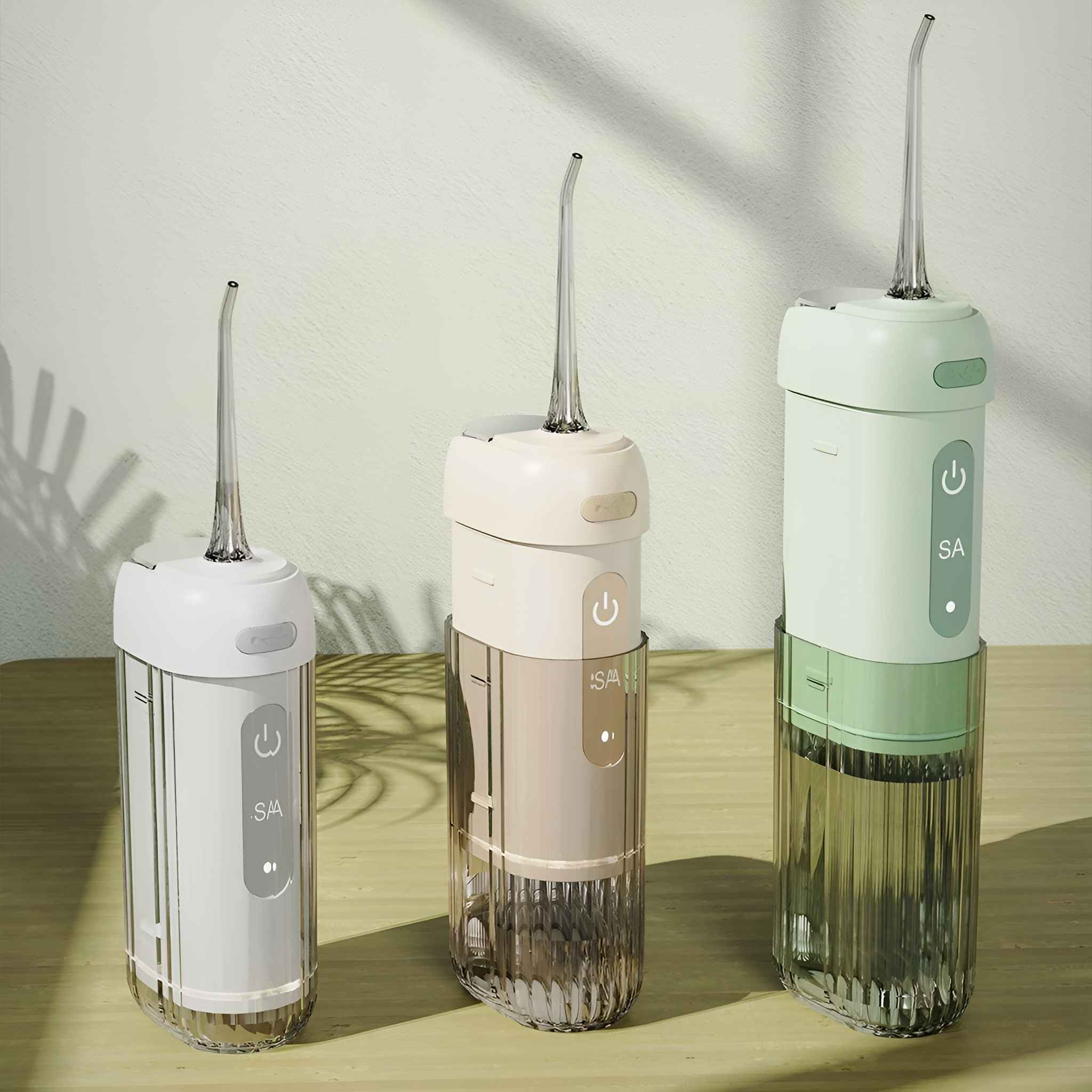 Drei Mundduschen, weiß, beige und grün. Sie haben klare Wassertanks und stehen auf einer Holzoberfläche.